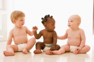 Three babies sitting indoors holding hands